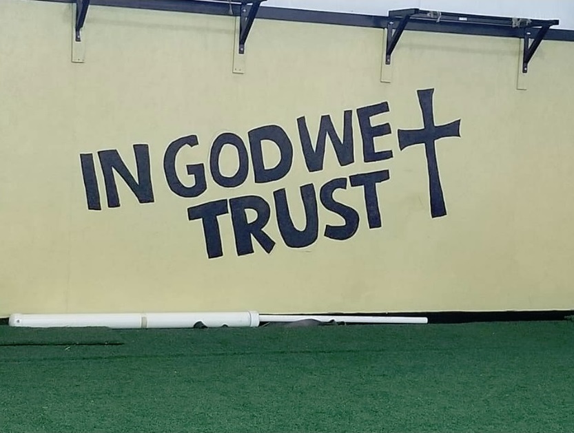 Photo of wall at a public school with "In God We Trust" and a cross.